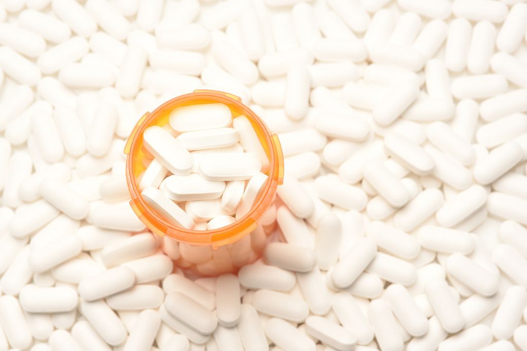 Concept of opiate library: high angle view of a prescription bottled filled with pills surrounded by more of the same tablets.