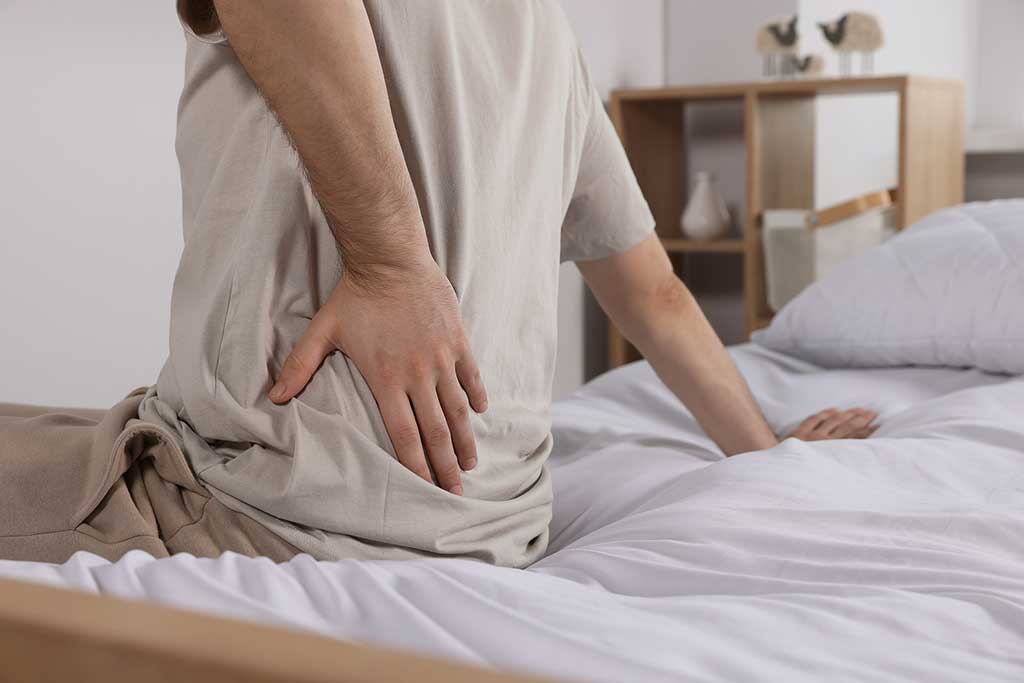 Man suffering from back pain while sitting on bed in room, closeup. Concept of sleep for patients with chronic pain.