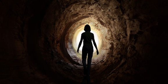 person standing inside a tunnel with a light showing at the end of the tunnel