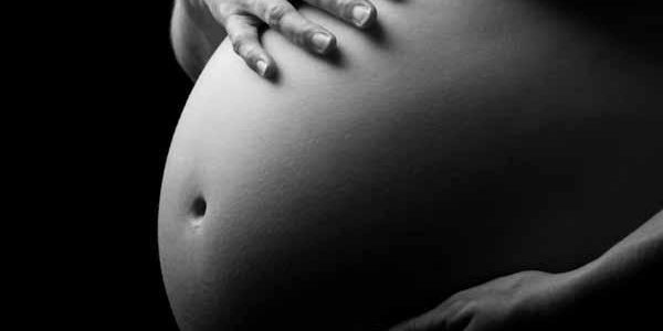 Black and white picture of pregnant stomach with woman holding the top and bottom of it.
