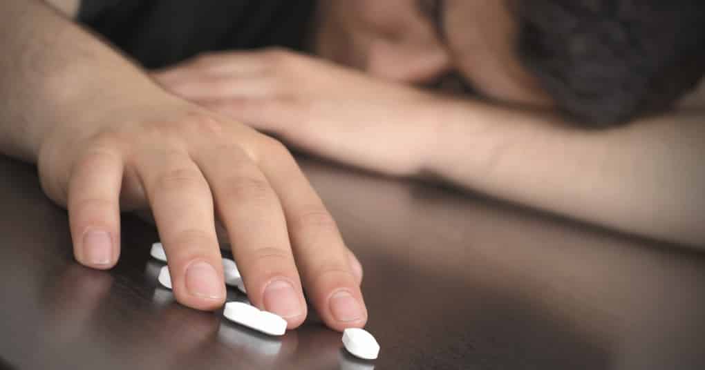 man laying on table with white opiate pills on table under one hand