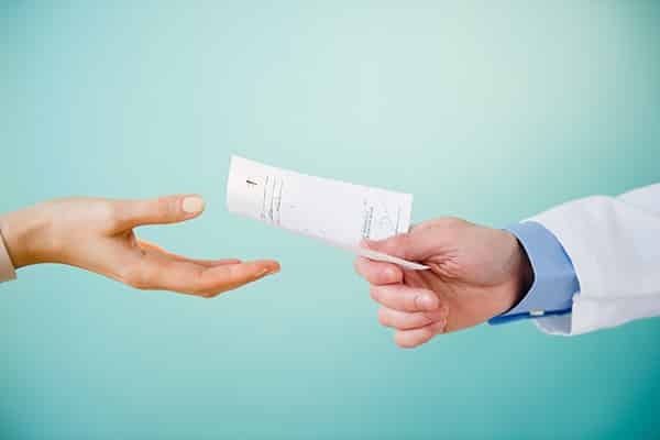 Dr. handing a woman a prescription. Only hands are visible.