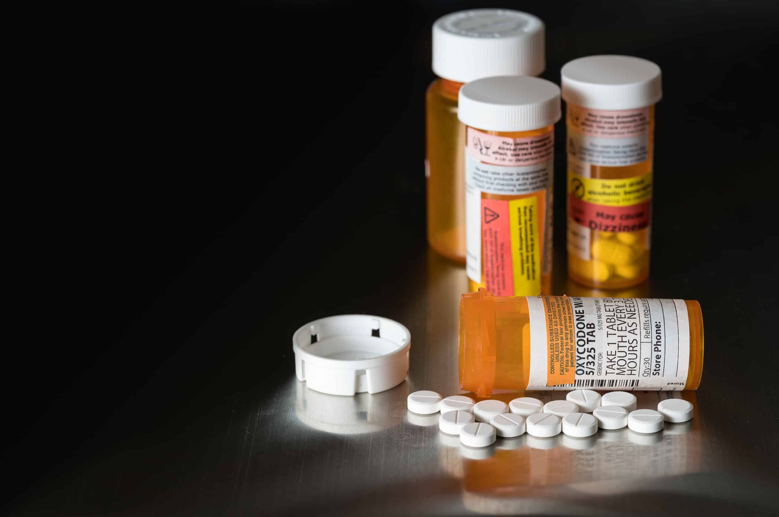 Oxycodone is the generic name for a range of opoid pain killing tablets. Prescription bottle for Oxycodone tablets and pills on metal table for opioid epidemic illustration