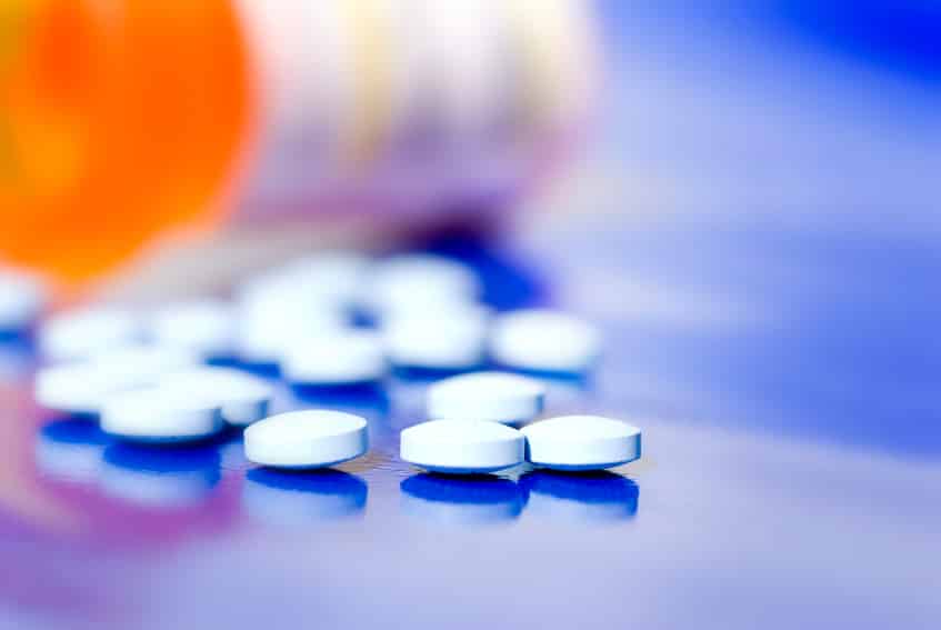 pills on blue surface with opened pill bottle blurred in the background. Illustration to bring to light fentanyl abuse.