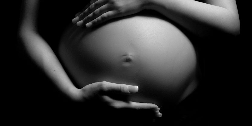black and white pregnant woman holding the top and bottom of her baby bump. Illustrates that every 25 minutes an infant is born positive to opioids