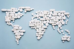 Flat map of the world made with white pills on a blue background. Illustrates the state of the acrylfentanyl public health emergency