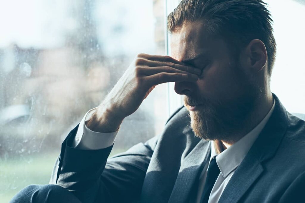 Man in suit with had clenching his upper nose bridge demonstrating stress