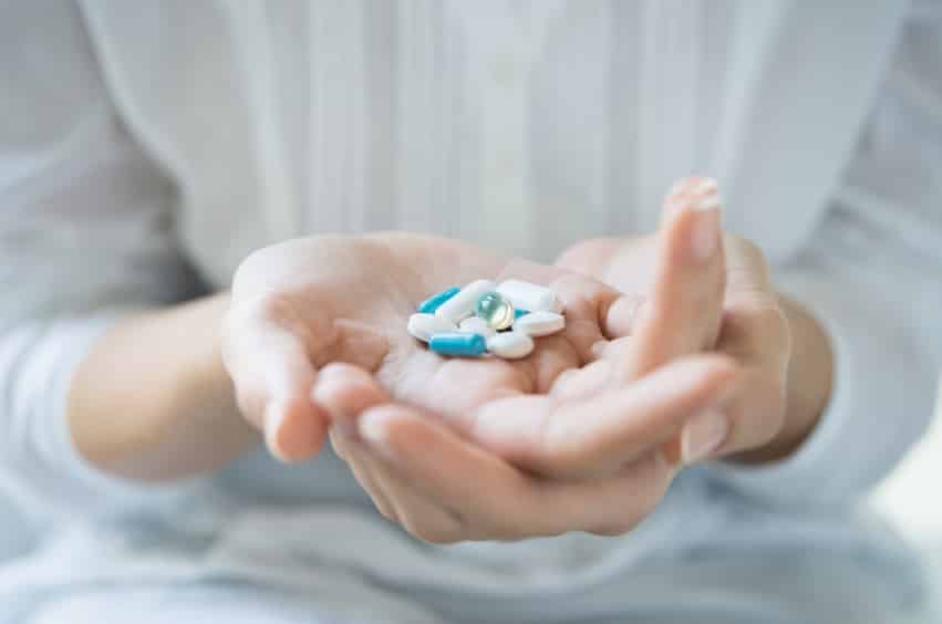 woman with hand held out and blue and white opioid pills within hand