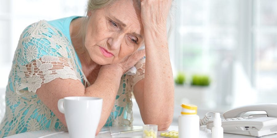 senior woman leaning on a kitchen counter with opioids on the table looking depressed.