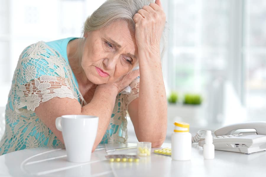 senior woman leaning on a kitchen counter with opioids on the table looking depressed.