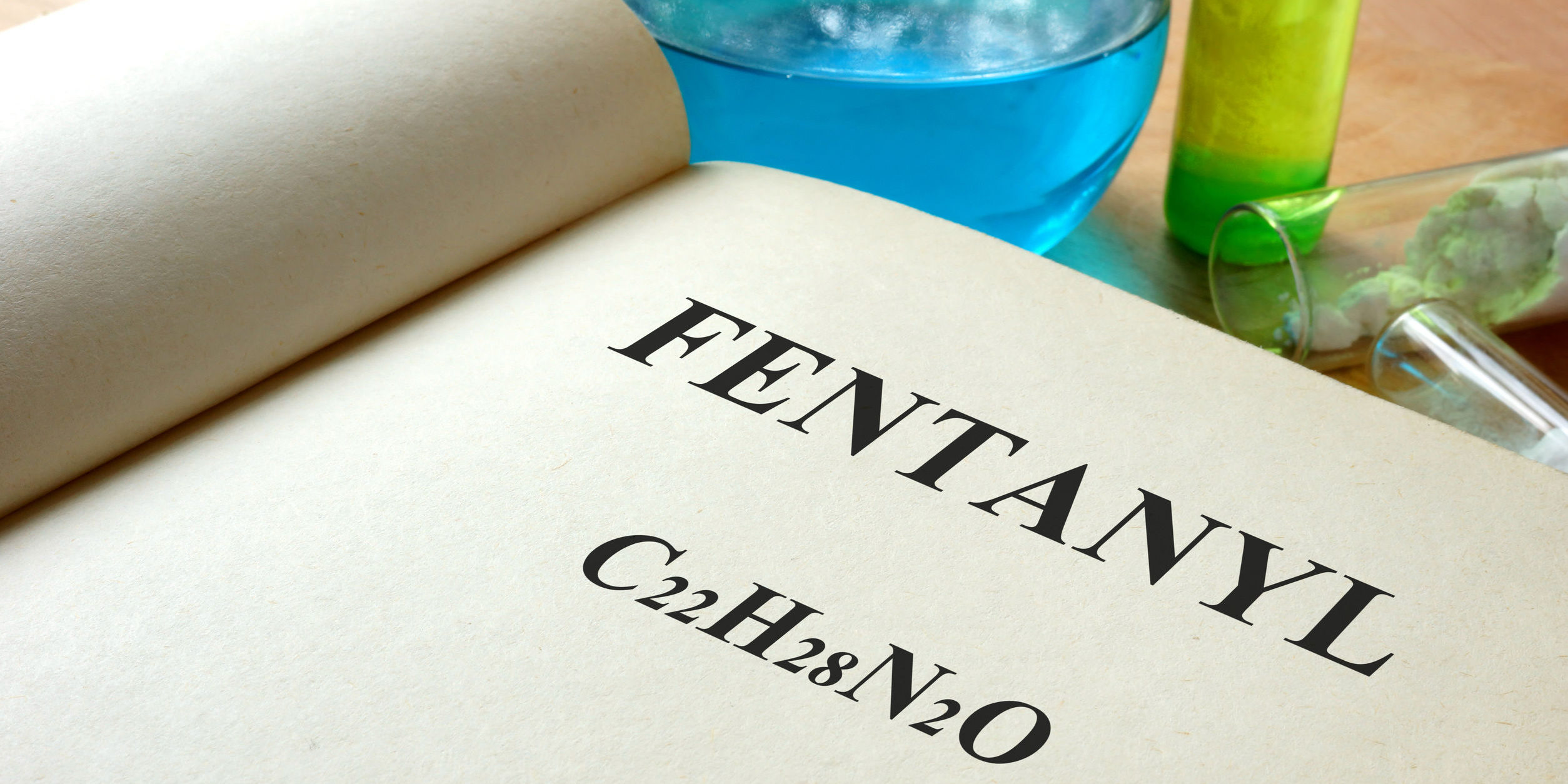 A book with fentanyl described and test tubes on a table illustrating pharmaceutical company creating fentanyl-based drugs