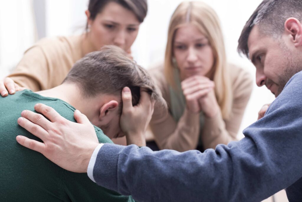 Close-up of a devastated young man battling opioid addiction holding his head in his hands during group therapy