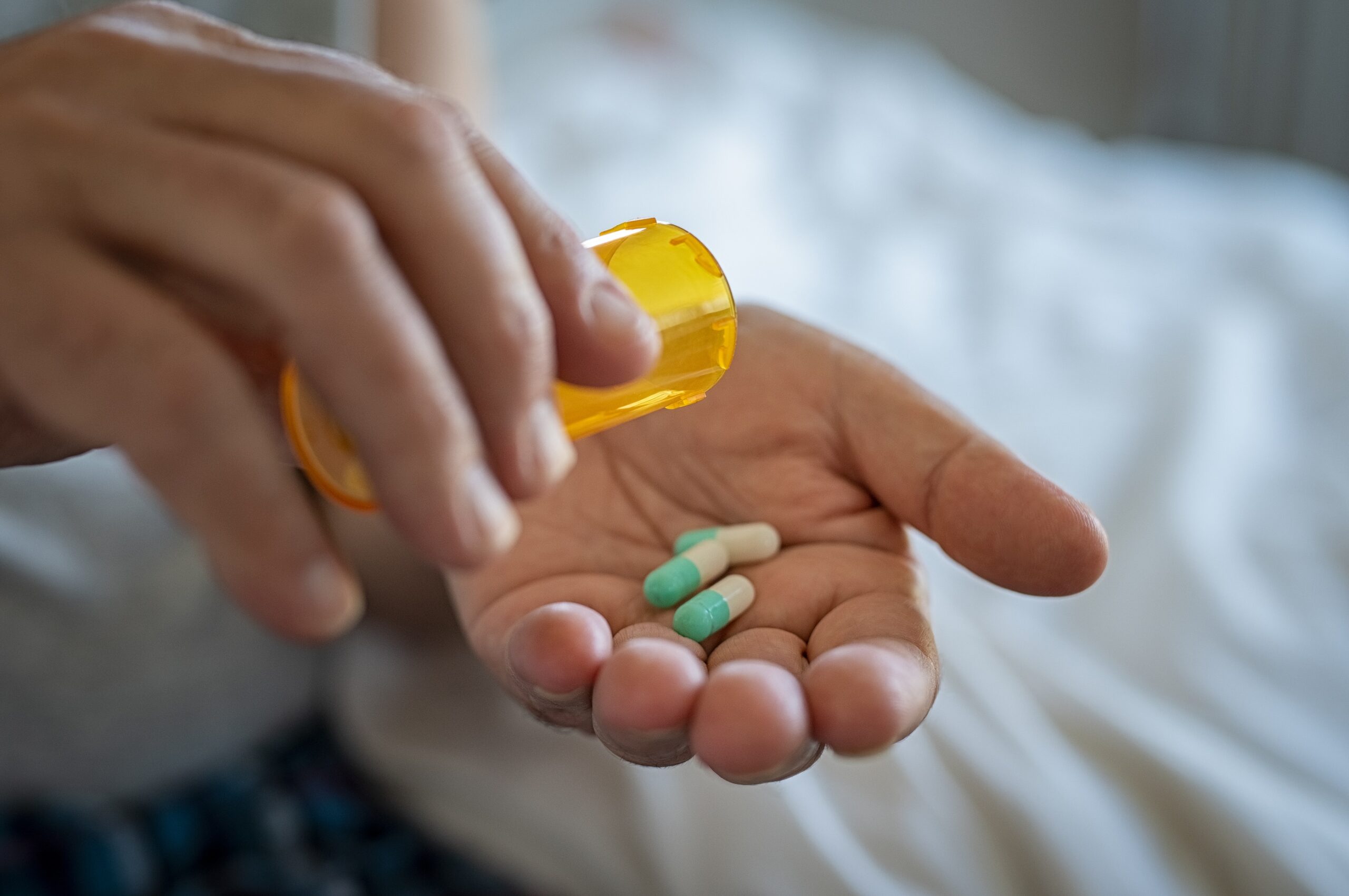 closeup of man pouring prescription pills into hand risking drug interactions between opioids and antidepressants