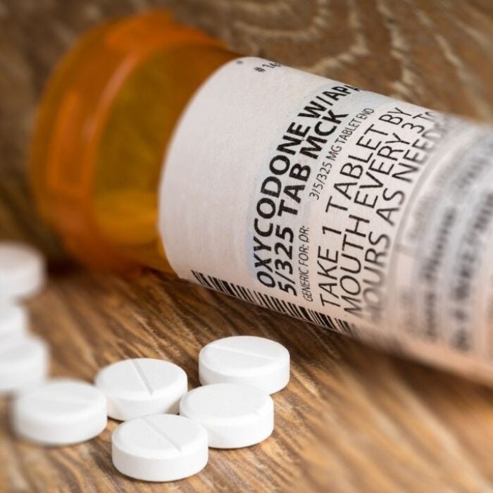 A close up photo of a prescription bottle for Oxycodone tablets and pills on wooden table. Concept of how to opioid detox safely.