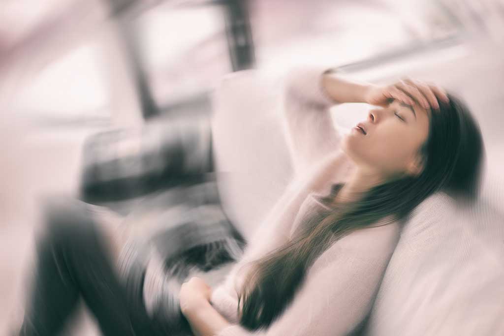 Sick woman with headache feeling faint vertigo holding head in pain with fever and migraine. Blurry motion blur background. Concept of oxycodone side effects