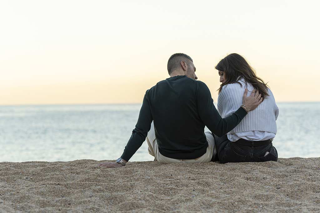 Man consoling his friend while sitting on the sand at the beach. Concept of a burnout in addiction recovery