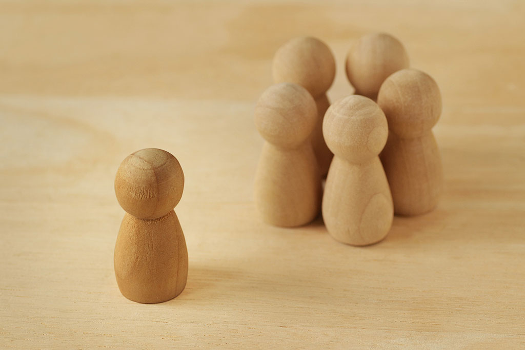 Wooden pawns representing group of people in circle and person alone - Concept of isolation and loneliness in addiction recovery