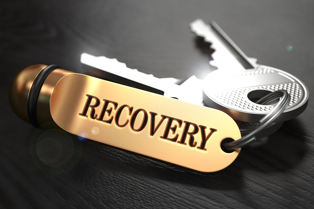 Overcoming Addiction Concept: Keys with a keychain with word Recovery on a golden label on a table - concept of