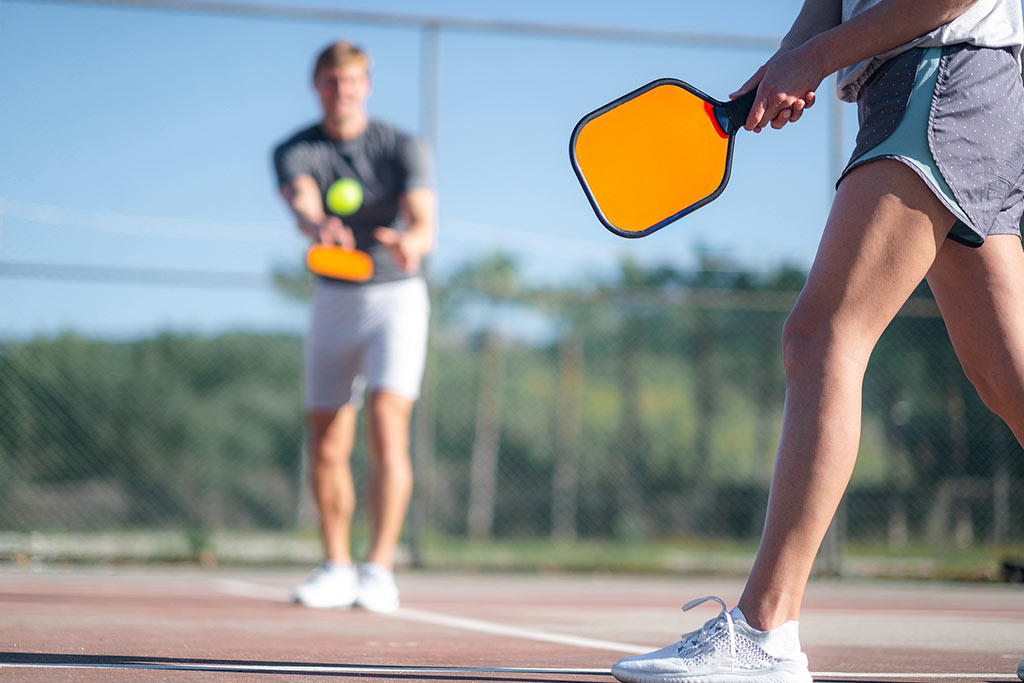 Concept of creating a supportive environment for addiction recovery: couple playing pickleball game, hitting pickleball yellow ball with paddle, outdoor sport leisure activity.
