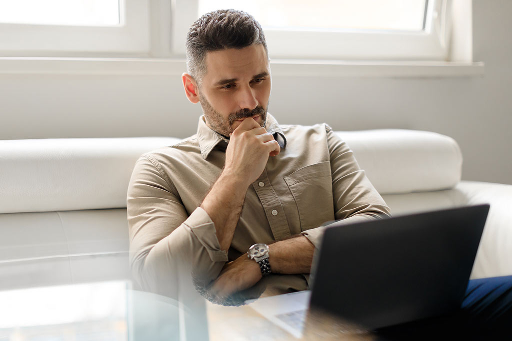 Focused thoughtful businessman using laptop and thinking of project, making decision, looking at computer screen - concept of a person researching options for opioid dependence treatment, such as rapid detox.