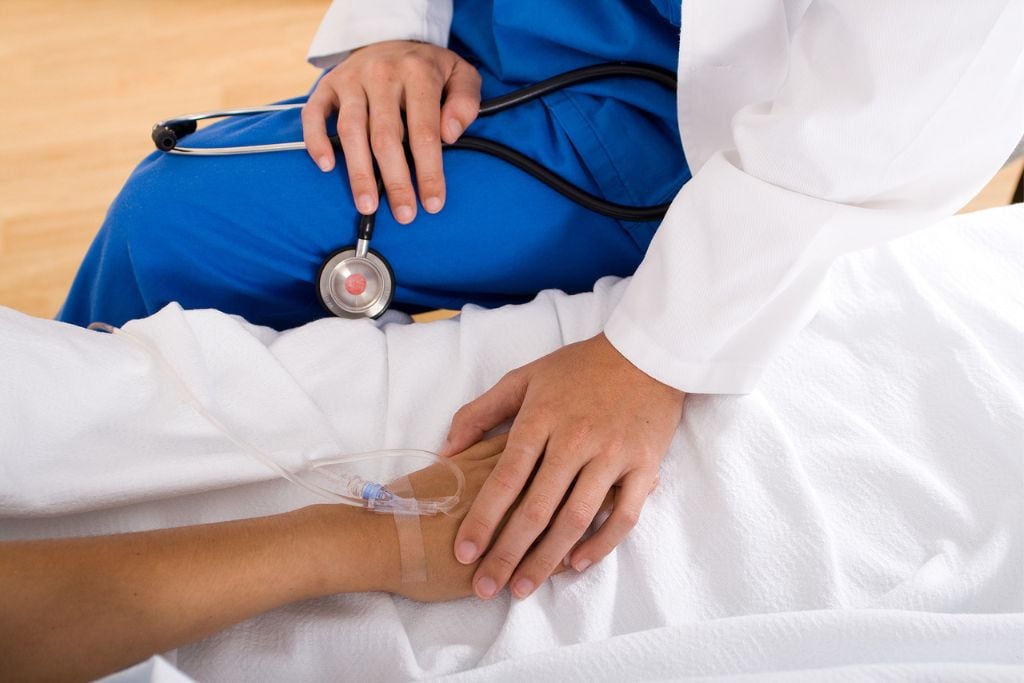 concept of sedated detox: photo of a medical professional comforting a patient with an IV in a hospital bed