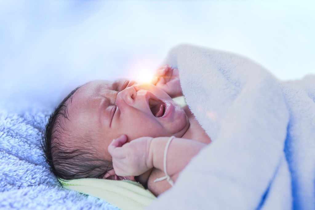 Newborn baby crying in bed under blue knit blanket. Concept of Neonatal Abstinence Syndrome (NAS)