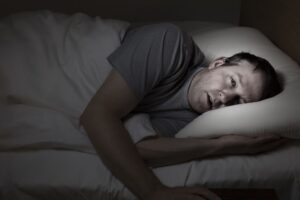 Mature man eyes wide open laying in bed experiencing withdrawal symptoms. Concept of opioid detox without medical supervision.