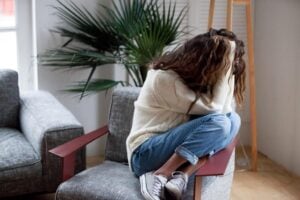Depressed sad woman holding head in hands sitting on armchair at home, harassment abuse teenage victim feeling bad, heartbroken upset girl crying having mental problem or dangerous drug addiction. Concept of women and drugs.
