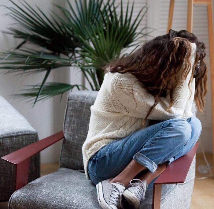 Depressed sad woman holding head in hands sitting on armchair at home, harassment abuse teenage victim feeling bad, heartbroken upset girl crying having mental problem or dangerous drug addiction. Concept of women and drugs.
